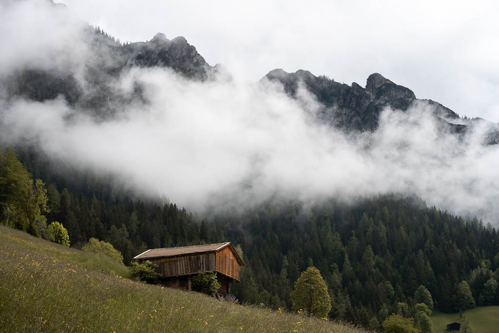 Wolken in den Bergen über einer Holzhütte in Alpbach