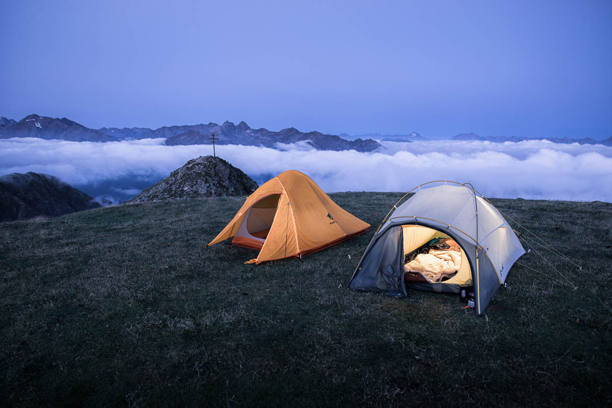Zwei zelten auf einer Wiese über den Wolken in den Alpen am Gipfelkreuz auf 2600m Höhe