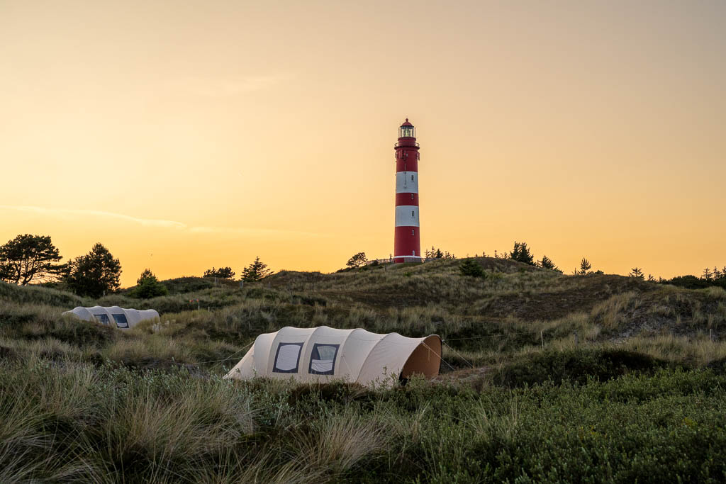 Leuchtturm Amrum zum Sonnenuntergang mit Zelten vom Campingplatz in den Dünen