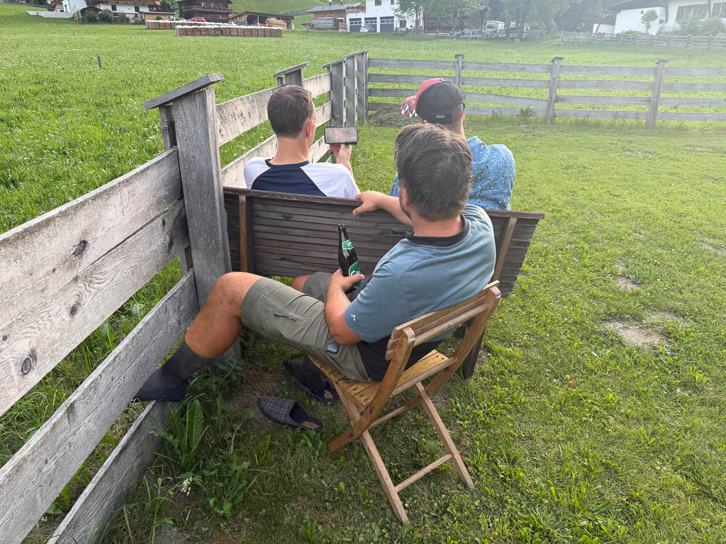 Die Wandergruppe sitzt am Abend im Garten und schaut gemeinsam Fußball auf dem Smartphone.