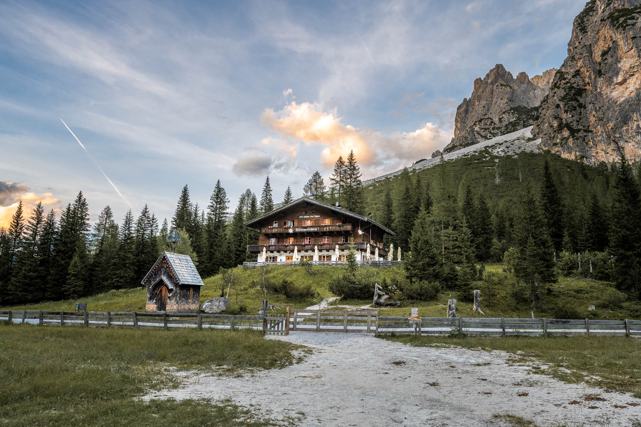 Die Dreischusterhütte liegt vor einer steilen Felskulisse am Rand einer Wiese