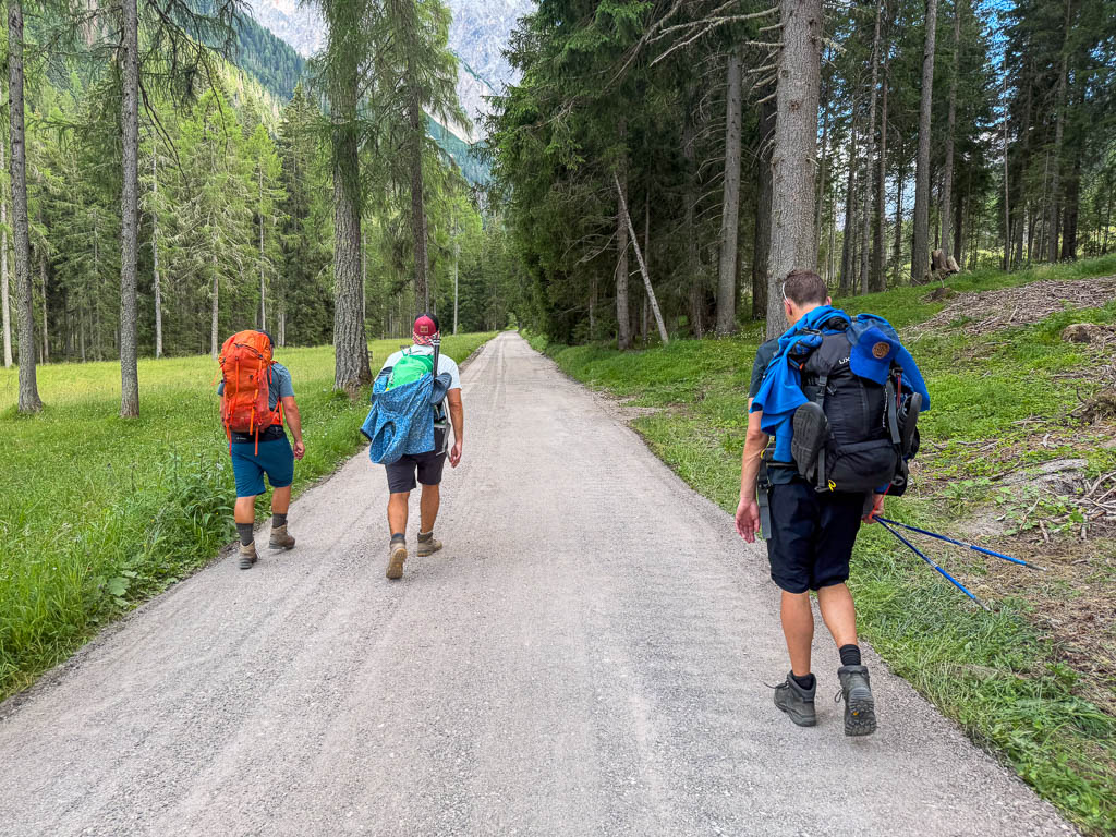 Drei Wanderer gehen auf einem breiten Weg durch den Wald in Richtung Dreischusterhütte