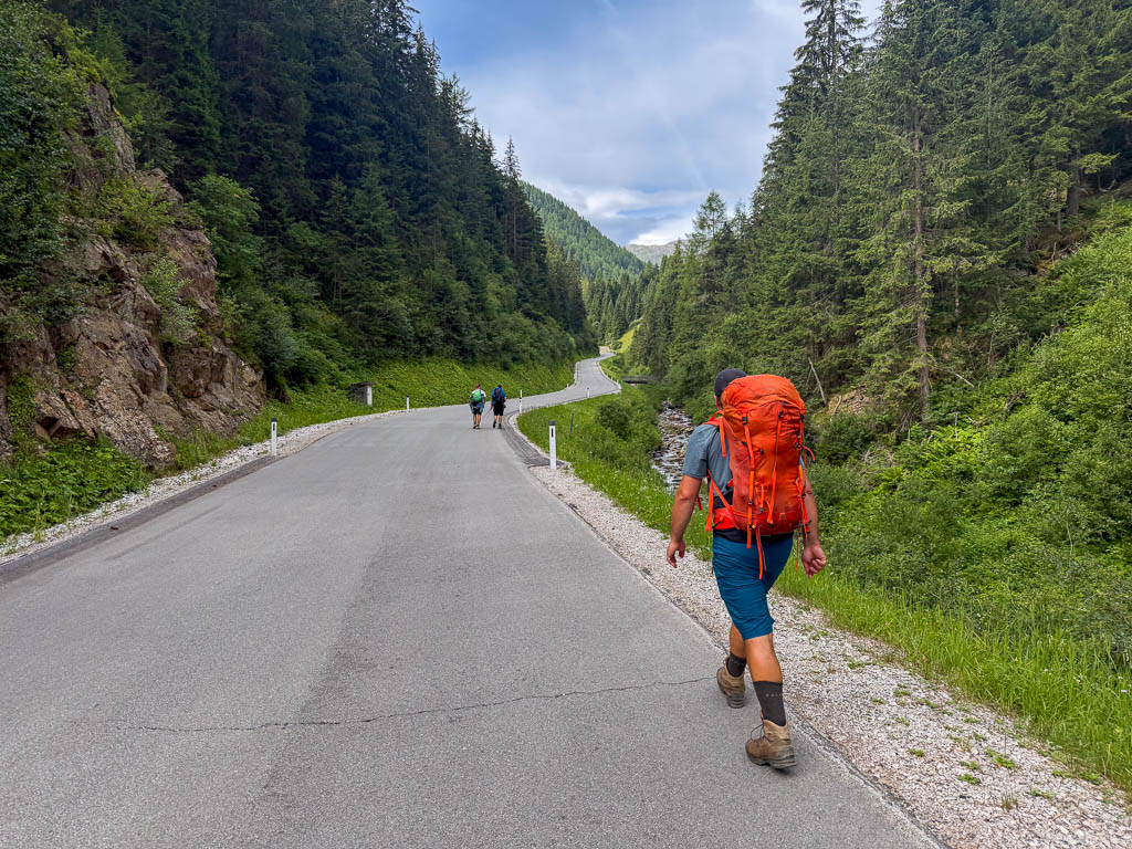 Wanderer mit rotem Rucksack auf der Straße durch das grüne Tal