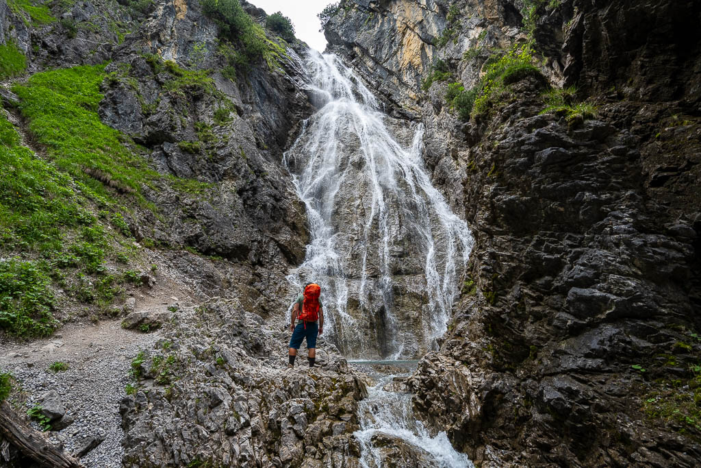 Wanderer mit Rucksack vorm Rossgumpen Wasserfall
