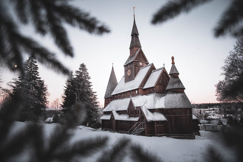 Stabkirche Hahnenklee zum Sonnenaufgang im Schnee mit Tannenzweigen